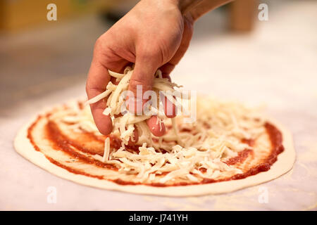 Cucinare mano versando il Formaggio per pizza in pizzeria Foto Stock