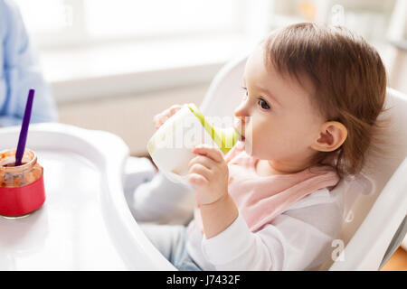 Baby bere dal bicchiere del tubo di lancio nel seggiolone a casa Foto Stock