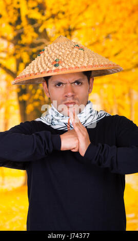 Ritratto di un bel giovane ispanica business ragazzo indossa un asiatico cappello conico facendo un saluto tradizionale con le sue mani nella collezione autunno sfondo Foto Stock