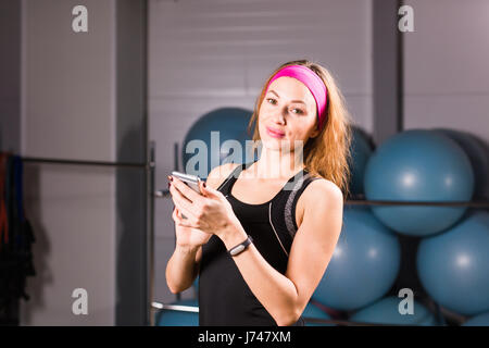 Sport e fitness, la tecnologia e le persone concetto - giovane donna con attività tracker e smartphone in palestra Foto Stock