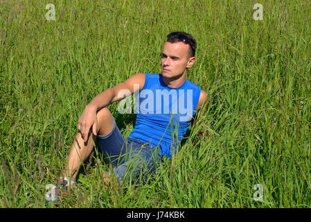 Un giovane uomo si siede nella folta erba verde nella giornata di sole . Foto Stock