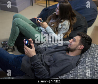 Coppia felice amici per giocare con i videogiochi con joystick seduto sulla poltrona sacco Foto Stock