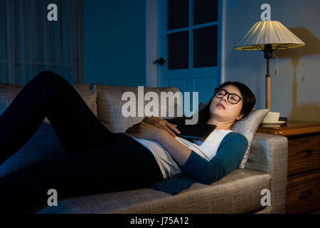 Giovane imprenditrice che dorme sul divano dopo il lavoro con la telefonia mobile digitale compressa computer sovraccaricando la notte sensazione molto stanco del riposo nelle liv Foto Stock