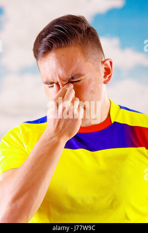 Giovane uomo ecuadoriana indossando maratona ufficiale Football Shirt in piedi di fronte alla fotocamera, molto impegnato il linguaggio del corpo la visione di gioco con grande entusiasmo, cielo blu e nuvole sullo sfondo Foto Stock