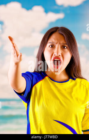 Giovane donna ecuadoriana indossando maratona ufficiale Football Shirt in piedi di fronte alla fotocamera, molto impegnato il linguaggio del corpo la visione di gioco con grande entusiasmo, cielo blu e nuvole sullo sfondo Foto Stock