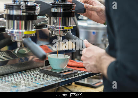 Il caffè nella macchina da caffè. Mani dell'uomo si prepara il caffè espresso fresco si riversa nella tazza di porcellana. Servizio di catering e di concetto Foto Stock