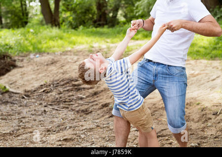 Irriconoscibile padre con piccolo figlio nel verde dei boschi, giornata di sole. Foto Stock