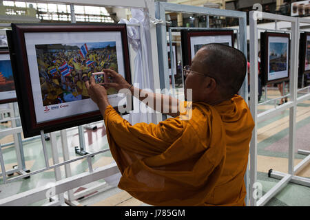 Una mostra fotografica di eventi del passato che celebra la fine Bhumibol Adulyadej Re di Thailandia. Un monaco ricattura l'immagine all'interno di un'immagine. Foto Stock