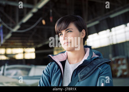 Fiducioso giovane pilota femmina che pongono in hangar aereo sullo sfondo Foto Stock