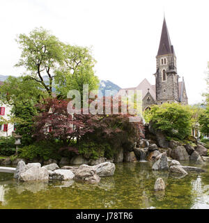 Un ornamentali giardino giapponese a Interlaken in Svizzera. La guglia della Schlosskirche (Castello) chiesa sorge in background. Foto Stock