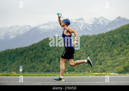 Rosa Khutor, Russia - 7 Maggio 2017: uomo guida sul punto di acqua si riversa faccia da una bottiglia d'acqua in gara Spring Mountain marathon Foto Stock