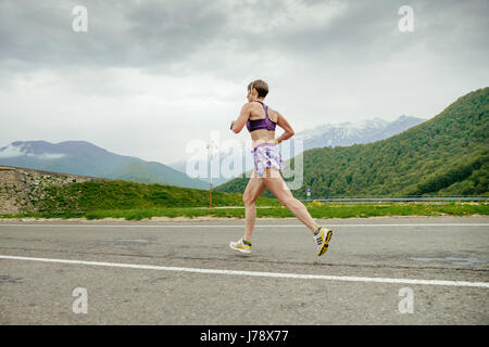 Una donna di mezza età runner in esecuzione su strada asfaltata in gara Spring Mountain marathon Foto Stock