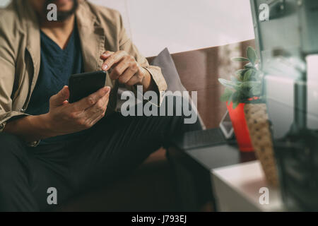 Hipster mano utilizzando smart phone,digitale compressa docking tastiera,tazza da caffè, pagamenti online business,seduto sul divano nel soggiorno,lavoro a casa concep Foto Stock