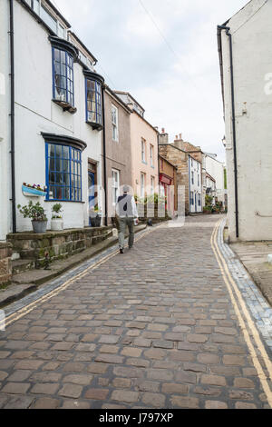 Un uomo cammina lungo le strade acciottolate e tortuose di Staithes, North Yorkshire, Regno Unito Foto Stock