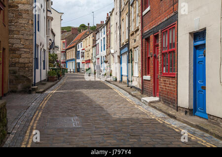 Un uomo cammina lungo le strade acciottolate e tortuose di Staithes, North Yorkshire, Regno Unito Foto Stock