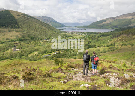 Glencoe village e Loch Leven visualizza - due escursionisti guardando alla vista di Glencoe villaggio dal sentiero che conduce fino al pap di Glencoe, Scozia Foto Stock