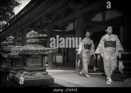 Foto in bianco e nero di due giovani donne che indossano i loro furisode di Nara. Sono passato di risveglio alcune lanterne di pietra. Foto Stock