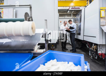 Conversazione tra due uomini tra le macchine in fabbrica e negozio Foto Stock