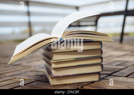 Pila di libri antichi sulla terrazza sullo sfondo di legno, uno superiore è aperto Foto Stock