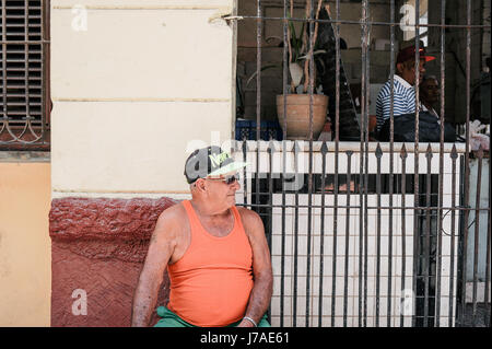 Il vecchio uomo cubano seduti sulle strade di l'Avana con una New York berretto da baseball Foto Stock
