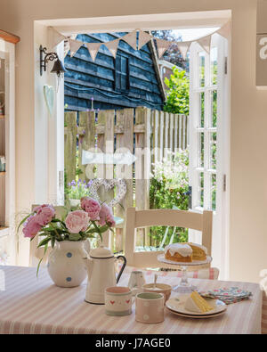 Pan di spagna, smalto teiera e peonie rosa sul tavolo rigato stoffa da Susie Watson Designs Foto Stock