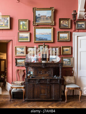 Una collezione di Julian Barrow dipinti sopra una in stile Tudor premere. Le pareti sono dipinte in Farrow & Ball il Libro rosso in camera Foto Stock