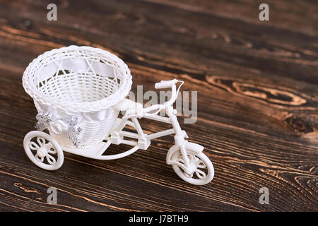 Triciclo in plastica cesto fiorito. Giocattolo bianco su marrone del legno. Foto Stock