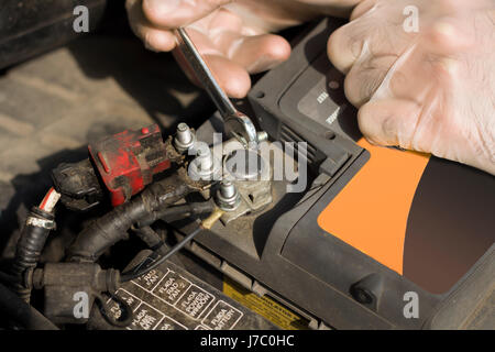 Le mani del meccanico di automobili in guanti monouso svitare la batteria frizione. La mano di un meccanico con una chiave piatta si svita la batteria in auto. Foto Stock