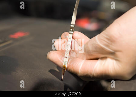 L'uomo le mani in guanti monouso per controllare il livello di olio nel motore. Foto Stock