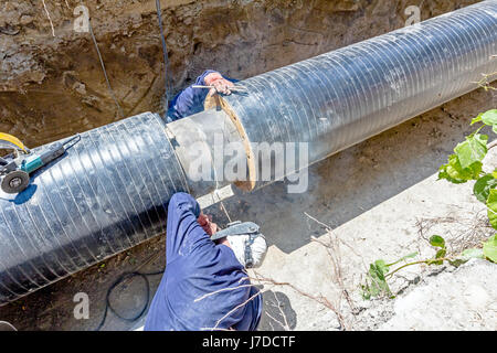 Il team di saldatori è in trincea lavorando duro per installare un nuovo gasdotto. Saldatura ad arco tubi Foto Stock