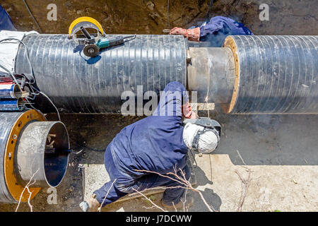 Il team di saldatori è in trincea lavorando duro per installare un nuovo gasdotto. Saldatura ad arco tubi Foto Stock