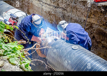 Il team di saldatori è in trincea lavorando duro per installare un nuovo gasdotto. Saldatura ad arco tubi Foto Stock