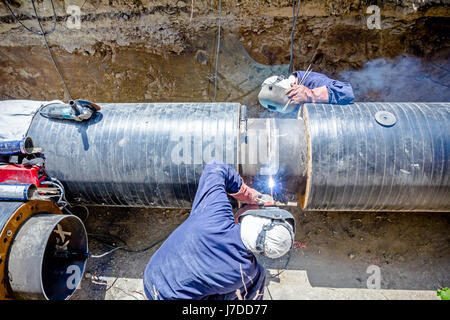 Il team di saldatori è in trincea lavorando duro per installare un nuovo gasdotto. Saldatura ad arco tubi Foto Stock