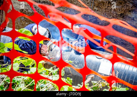 I saldatori sono in trincea che operazioni di saldatura ad arco pipeline. Spazio ristretto con Orange, plastica, rete di sicurezza Foto Stock