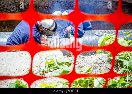 I saldatori sono in trincea che operazioni di saldatura ad arco pipeline. Spazio ristretto con Orange, plastica, rete di sicurezza Foto Stock