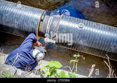 Il team di saldatori è in trincea lavorando duro per installare un nuovo gasdotto. Saldatura ad arco tubi Foto Stock