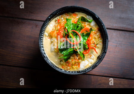 Una ciotola di maiale al curry con le foglie di basilico su un tavolo di legno Foto Stock