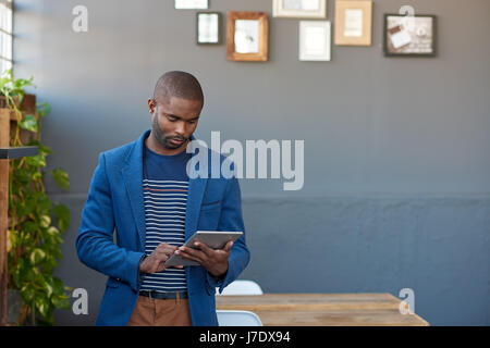 Focalizzato giovane imprenditore africani in piedi da solo in un grande ufficio moderno lavora online con una tavoletta digitale Foto Stock