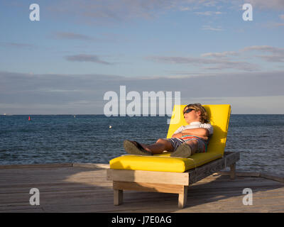 Un ragazzo prende un pisolino su un giallo chaise lounge su un molo durante il tramonto su Al Bitter End Yacht Club nelle Isole Vergini Britanniche off le isole Foto Stock