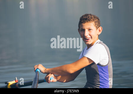 Un giovane singolo scull concorrente a remi pagaie sul tranquillo lago Foto Stock