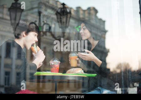 Foto di felice giovane uomo seduto in cafe con la sorella di bere succo di frutta mangiare panino. Guardando a parte. Foto Stock