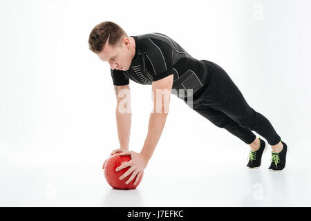 A piena lunghezza Ritratto di una giovane atleta sano uomo a fare gli esercizi con la pesante palla fitness isolate su sfondo bianco Foto Stock