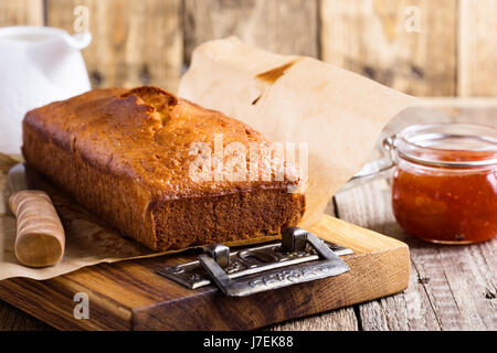 In casa ciambellone sulla carta da forno servita con marmellata di frutta pronto a mangiare sulla tavola in legno rustico, delizioso brunch o tea time Foto Stock