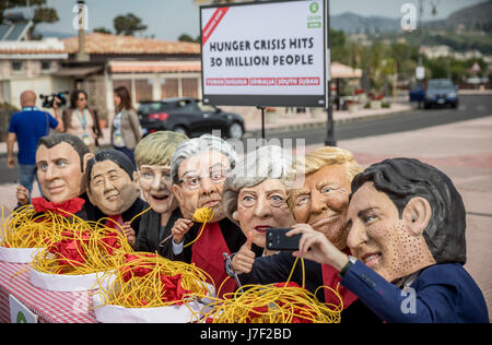 Taormina, Italia. 25 Maggio, 2017. Gli attivisti di Oxfam indossare maschere del G7-capi del presidente francese Emmanuel Macron (L-R), Giappone il Primo Ministro Shinzo Abe, Tedesco il Cancelliere Angela Merkel, Italia Il Ministro Presidente Paoplo Gentilono, Gran Bretagna il Primo Ministro Teresa maggio, US-presidente Donald Trump e Canada il Primo Ministro Justin Trudeau sedersi su un set di simbolicamente la tabella nella parte anteriore di piastre di spaghetti a Taormina, Italia, 25 maggio 2017. Credito: dpa picture alliance/Alamy Live News Foto Stock