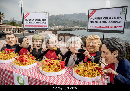 Taormina, Italia. 25 Maggio, 2017. Gli attivisti di Oxfam indossare maschere del G7-capi del presidente francese Emmanuel Macron (L-R), Giappone il Primo Ministro Shinzo Abe, Tedesco il Cancelliere Angela Merkel, Italia Il Ministro Presidente Paoplo Gentilono, Gran Bretagna il Primo Ministro Teresa maggio, US-presidente Donald Trump e Canada il Primo Ministro Justin Trudeau sedersi su un set di simbolicamente la tabella nella parte anteriore di piastre di spaghetti a Taormina, Italia, 25 maggio 2017. Credito: dpa picture alliance/Alamy Live News Foto Stock