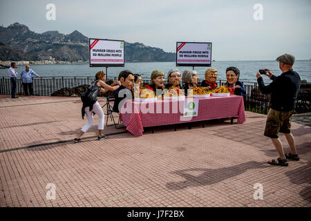 Taormina, Italia. 25 Maggio, 2017. Gli attivisti di Oxfam indossare maschere del G7-capi del presidente francese Emmanuel Macron (L-R), Giappone il Primo Ministro Shinzo Abe, Tedesco il Cancelliere Angela Merkel, Italia Il Ministro Presidente Paoplo Gentilono, Gran Bretagna il Primo Ministro Teresa maggio, US-presidente Donald Trump e Canada il Primo Ministro Justin Trudeau sedersi su un set di simbolicamente la tabella nella parte anteriore di piastre di spaghetti a Taormina, Italia, 25 maggio 2017. Credito: dpa picture alliance/Alamy Live News Foto Stock