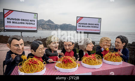 Taormina, Italia. 25 Maggio, 2017. Gli attivisti di Oxfam indossare maschere del G7-capi del presidente francese Emmanuel Macron (L-R), Giappone il Primo Ministro Shinzo Abe, Tedesco il Cancelliere Angela Merkel, Italia Il Ministro Presidente Paoplo Gentilono, Gran Bretagna il Primo Ministro Teresa maggio, US-presidente Donald Trump e Canada il Primo Ministro Justin Trudeau sedersi su un set di simbolicamente la tabella nella parte anteriore di piastre di spaghetti a Taormina, Italia, 25 maggio 2017. Con questa azione gli attivisti si desidera sollevare la consapevolezza per la carestia in Africa. Credito: dpa picture alliance/Alamy Live News Foto Stock