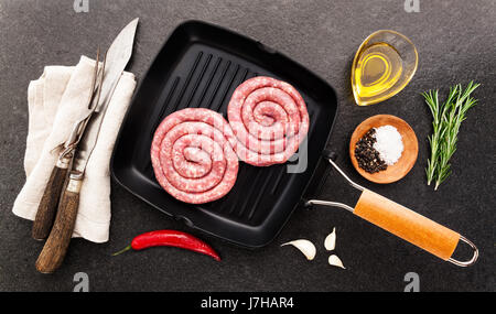 Materie insaccato di maiale con semi di finocchio in padella per grigliare con posate di taglio per sezionare e spezie Foto Stock
