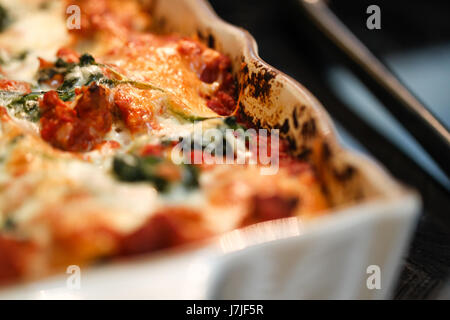 Primo piano. Al di fuori del forno-fresco, formaggio cotto lasagne, qui mostrato in un bianco smaltato piatto di cottura. Foto Stock