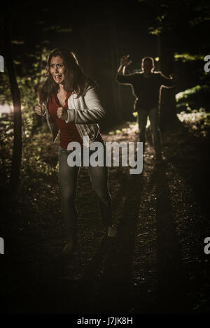 Giovane donna spaventata in esecuzione attraverso la foresta di notte in abito bianco e di scappare da uomo. Foto Stock